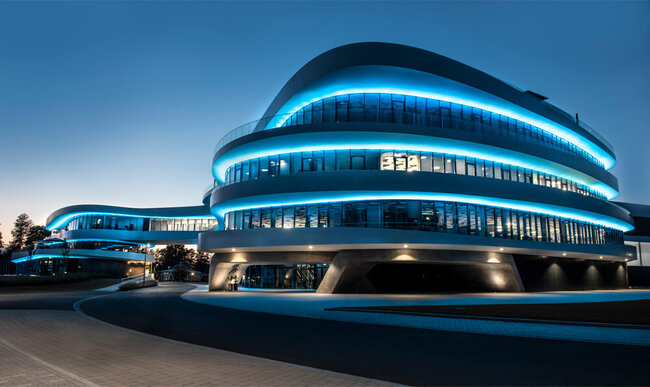 Nachtaufnahme: Ein Gebäude mit geschwungenen Formen und blauen Leuchteffekten.