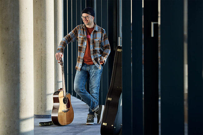 Karl Ruhland steht mit seiner Gitarre in einem Säulengang.
