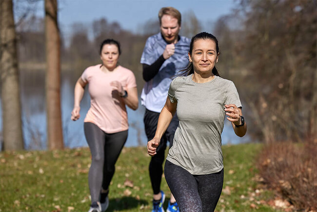Two women and one man are jogging on the banks of a lake.