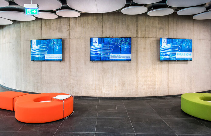 Ein Aufenthaltsbereich mit modernen Sitzelementen und mehreren Bildschirmen an der Wand.
