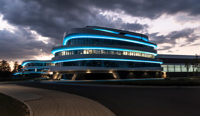 Nachtaufnahme: ein Gebäude mit geschwungenen Formen und blauen Leuchteffekten.