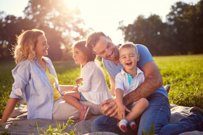 Familienszene: Eltern und zwei Kinder relaxen auf einer Wiese im Sonnenschein.
